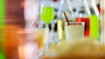 Tasty creamy spiced homemade eggnog drink with gingerbread in glass on middle of beverages table in Thanksgiving Christmas eve party surrounded by other alcoholic bottles liquor fries and snacks