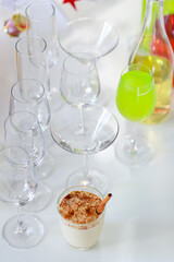 Tasty delicious milk cream eggnog drink with gingerbread in glass on table in front empty tall wine glasses present gift boxes white chocolate candles green apple punch and decorated Christmas tree