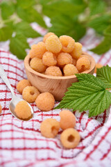 Malina żółta w drewnianej miseczce na ściereczce i z liśćmi w tle