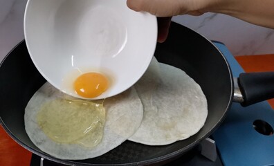 Pouring Raw Egg on top of Tortilla Wraps inside a Frying Pan