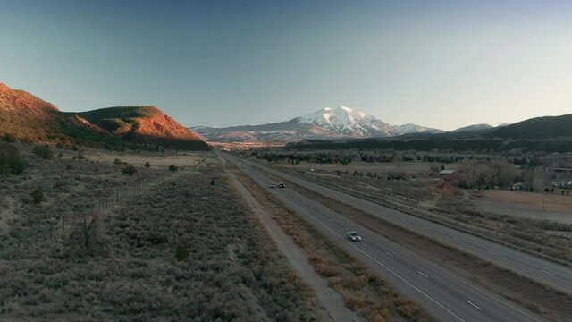 Aerial: Country highway traffic and Mt Sopris at sunset. Carbondale, Colorado, USA
