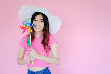 Portrait beautiful asian teen girl wearing pink dress on pink background, fashion summer set with colorful wind turbine or pinwheel or wind toy holding in hand,  emotions action, happy life concept