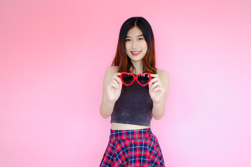 Portrait beautiful asian cheerful girl and beaming smile with red heart shaped sunglasses fashion eyewear on pink background, emotions action, happy summer life concept