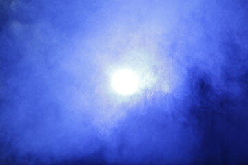 Artificial magic smoke in blue light on black background