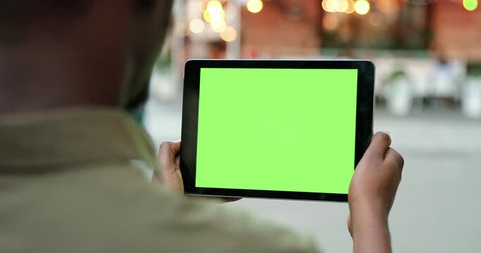 Male hands holding tablet with green screen. Guy using mobile phone while walking in the autumn street. Back view shot. Chroma key, close up man hand holding device with vertical green screen