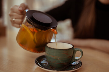 Woman pouring sea buckthorn tea in close-up. Women’s hands holding a teapot with tea and pour tea into a mug. 