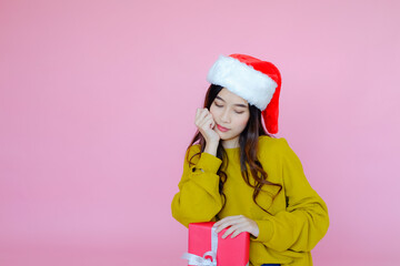 posing asia woman wearing long sleeve clothes on pink background with Santa Claus hat and red gift box holding in hand, holiday in festive Christmas or X'mas and happy new year concept, Winter fashion