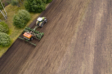 Aerial view of agricultural tractor with seeder machine at work on the field	