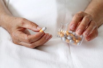 Pills in wrinkled hands of elderly woman sitting in a bed. Medication in capsules, taking sedatives, antibiotics or vitamins in old age