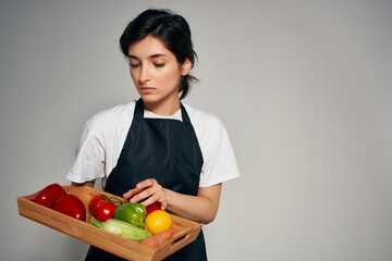 Woman in black apron holding a tray with fresh vegetables