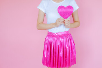 Portrait beautiful asian teen girl wearing white T-shirt and pink skirt on pink background, happy valentine day in love concept, model holding red heart sign in hand