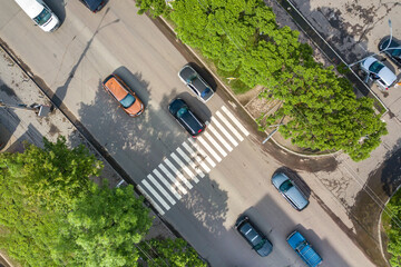 Top down aerial view of busy street with moving cars traffic and zebra road pedestrian crosswalk.