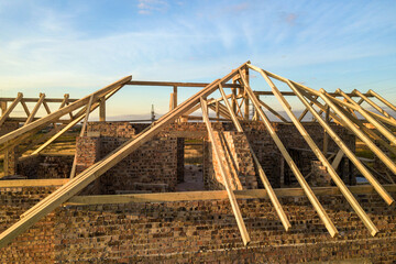 Private residential house with wooden roof frame structure under construction. Unfinished brick building under development.