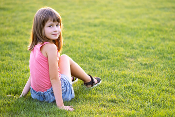 Fototapeta premium Young pretty child girl laying down on green grass lawn on warm summer day.