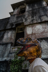 Unrecognizable dinosaur head mask against horror ruined abandoned house