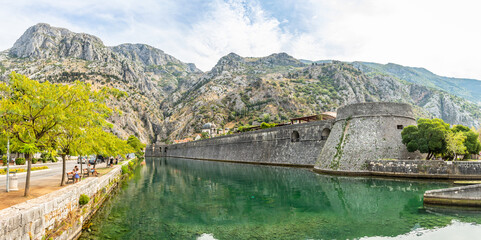 Fototapeta na wymiar Kampana tower and medieval fortress walls with mountains and Scurda river green waters in the foreground, Kotor Bay, Montenegro