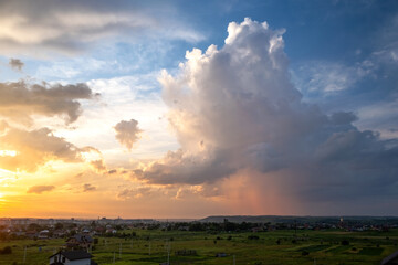 Dramatic sunset landscape of rural area with stormy puffy clouds lit by orange setting sun and blue sky.