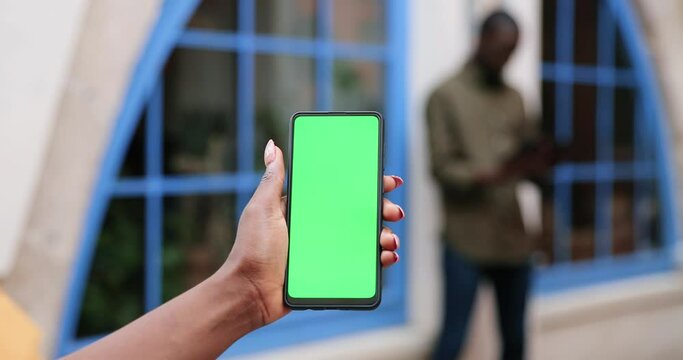 Female hands holding smartphone with green screen. Girl using mobile phone while walking in the autumn street. Back view shot. Chroma key, close up woman hand holding phone with vertical green screen