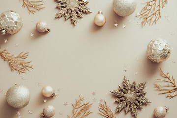 Christmas frame with golden snowflakes, Xmas tree branches, balls on beige background. Flat lay, top view.