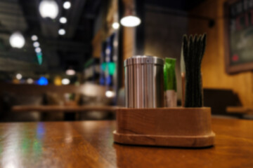 Defocused photo of the interior of a restaurant, pub, cafe. Spices shaker and napkins in a wooden stand in the foreground.