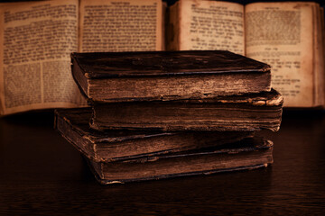 Stack of old worn shabby jewish books in leather binding and open blurred Torah in the background in the dark. Closeup. Selective focus.