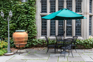 Wrought iron table and chairs on patio with turquois umbrella against large window and vine covered wall.  Romantic and charming gathering spot.