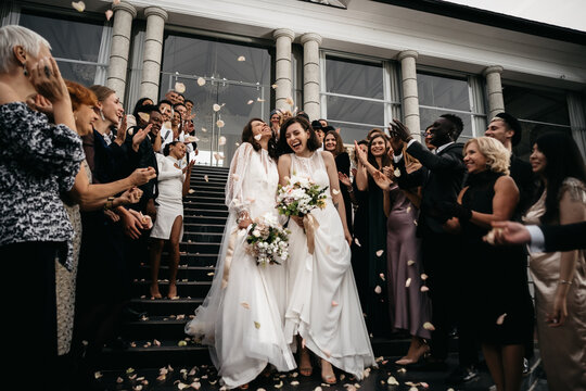 Candid shot of two female lesbian LGBT brides walking down the stairs during their wedding ceremony as guests throwing rose petal