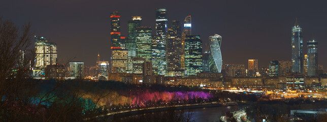 Long exposure photography of Moscow cityscape during winter night. Cold weather. Blurred lights of the city. Bright lighting of Moskva river embankment. Skyscrapers of Moscow business district