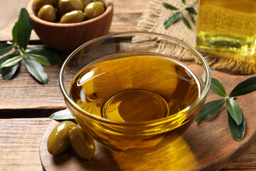 Glass bowl of oil, ripe olives and green leaves on wooden table, closeup