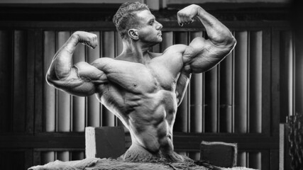 Brutal and muscular strong bodybuilder athletic man pumping up muscles at workout in the gym. Sport and health care concept background