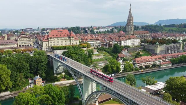 Aerial drone footage of tram cars driving on the Kirchenfeld bridge above the Aar river in Bern old town with the cathedral in Switzerland capital city.