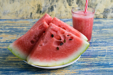 Sweet watermelon sliced on a white plate and watermelon smoothie in a glass glass.
