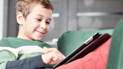 Cheerful little boy smiling while sitting on couch and using tablet at home. Modern kid and education technology. little boy looking at touch pad at home.
