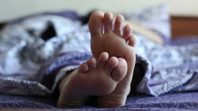 The girl makes plans for the day lying in bed. Beautiful female feet, standing one on top of the other.