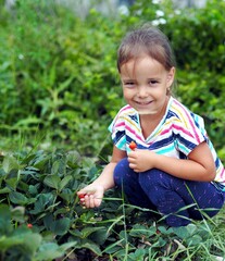 Communication with nature. Natural food. A little girl sits in a bed with berries and rejoices.