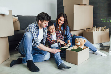 Beautiful happy family bout a house. Moving concept. Happy  couple with cardboard box and son reading a book!