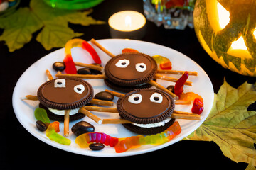 Themed Halloween dessert decor in the form of spiders made of chocolate cookies, sweet sticks and white glaze for the eyes. An example of a treat for the decor of a festive party table for Halloween.