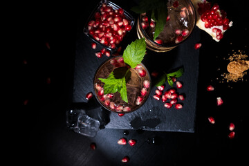 two colorful summer cocktails with pomegranate and mint on a black table