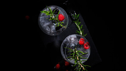 two gin tonc with berry and rosemary on a balck background