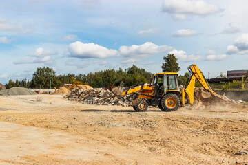 An excavator in a bucket transports soil for backfilling at the construction site. Construction equipment for earthworks.