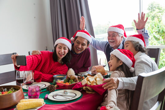 Happy Asian family wearing Santa red hat have lunch and take a photo together on Christmas day at home. Merry Christmas and Happy Holidays. Christmas holiday celebration