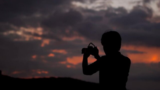 Silhouette of an Indian photographer taking photos with his camera during the sunset. Man taking pictures with his camera during the sunset. Photographer takes out his camera and takes photo. 