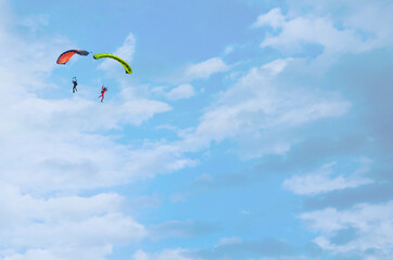 two men glide with a parachute against the background of a blue sky with white clouds, two parachutists