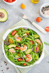 Delicious fresh salad with prawns, tomatoes, avocado, cucumber and onions in a bowl on a gray concrete background. Healthy dish. Top view, copy space.