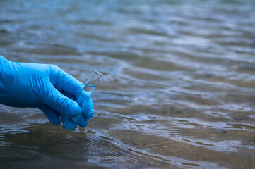 A man's hand in a blue glove takes a close-up of water into a test tube to measure water pollution....