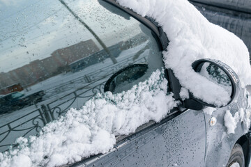 Car is covered with white snow. Glass with water drops, reflection. Winter season concept, snow cyclone.