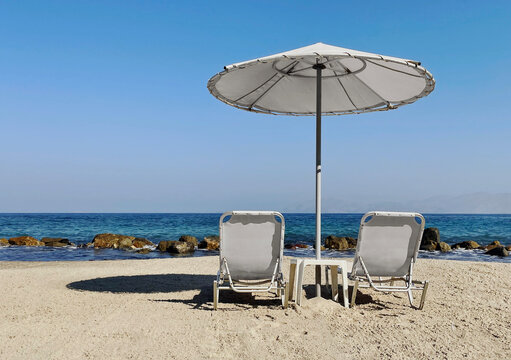 Zwei leere Sonnenliegen mit Sonnenschirm am Strand von Griechenland, horizontal