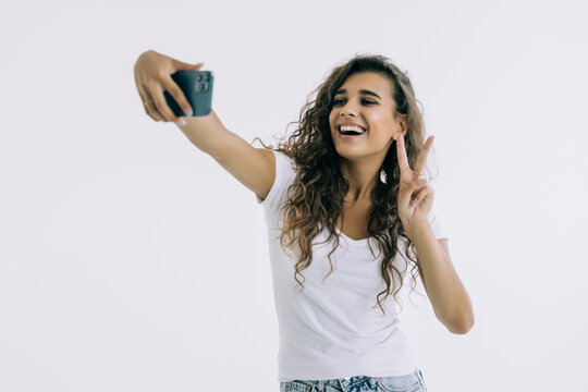 Portrait of a young attractive woman making selfie photo on smartphone on a white background
