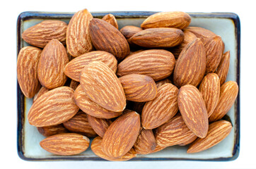 Closed up dry organic almond seed pile in ceramic bowl isolated on white background