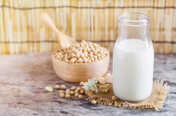 Closed up fresh organic homemade soybean milk in glass bottle over blur soybean seed pile in wooden bowl and spoon on grunge background in soft light tone